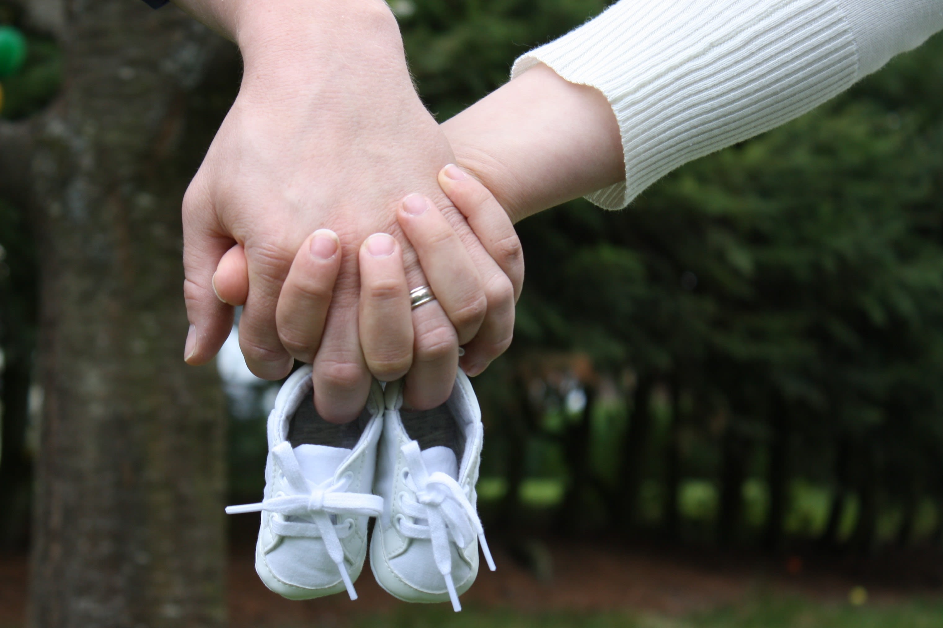 A MARRIED COUPLE HOLDING HANDS AND A PAIR OF BABY SHOES